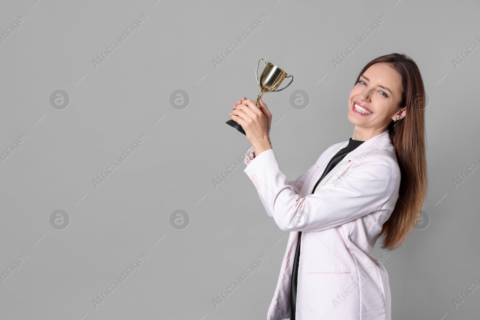 Photo of Happy winner with gold trophy cup on gray background, space for text