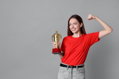 Happy winner with gold trophy cup on gray background, space for text