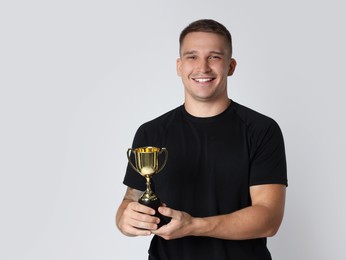 Happy winner with golden trophy cup on light grey background, space for text