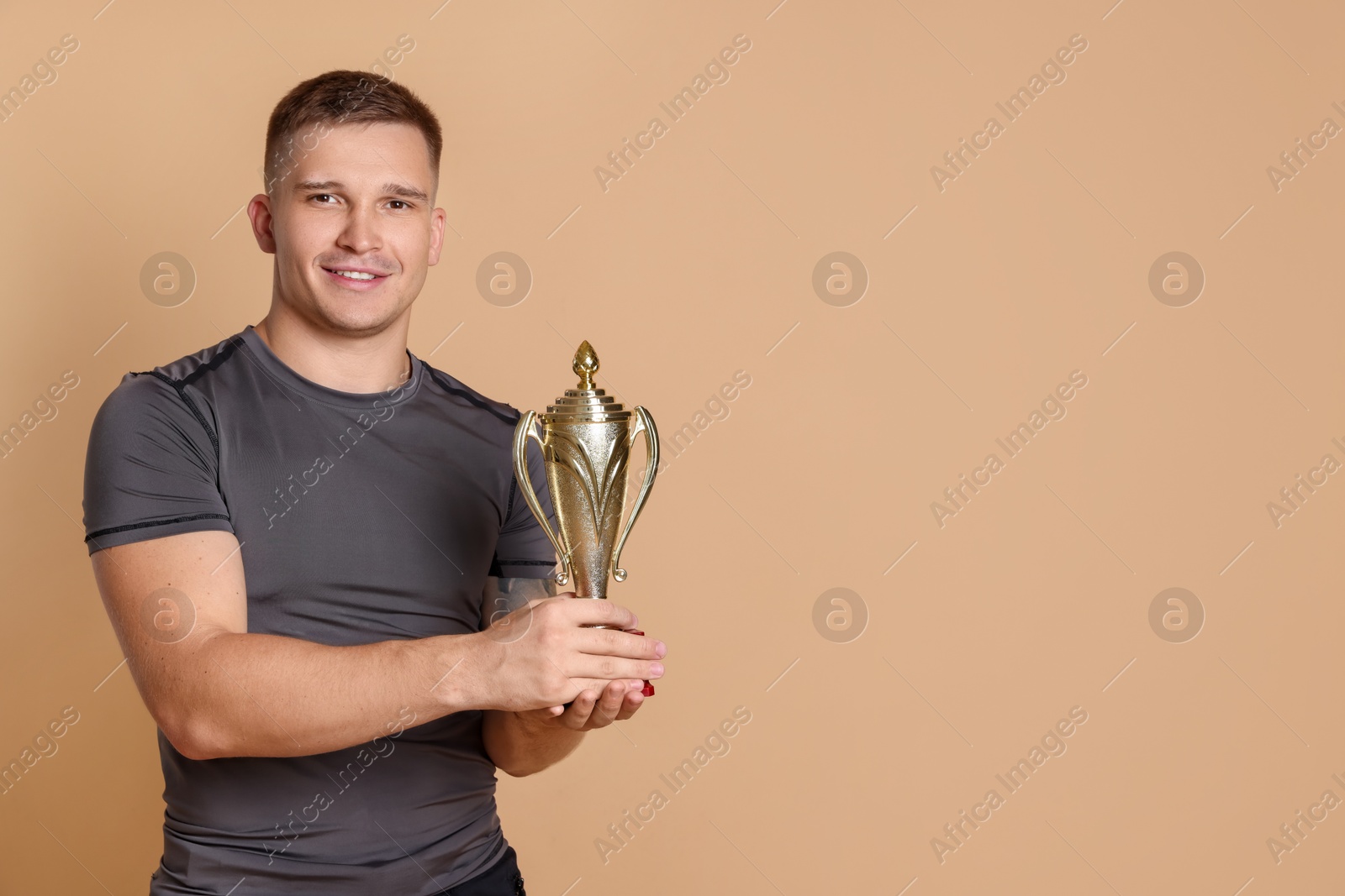 Photo of Happy winner with golden trophy cup on beige background, space for text