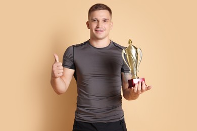 Photo of Happy winner with golden trophy cup showing thumbs up on beige background