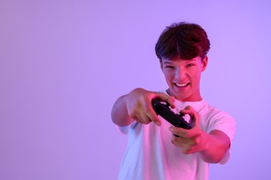 Teenage boy playing video game with controller on violet background. Space for text