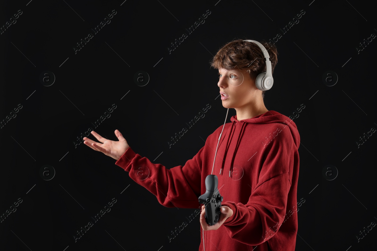 Photo of Teenage boy in headphones with controller on black background. Space for text