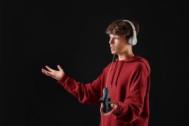 Teenage boy in headphones with controller on black background. Space for text