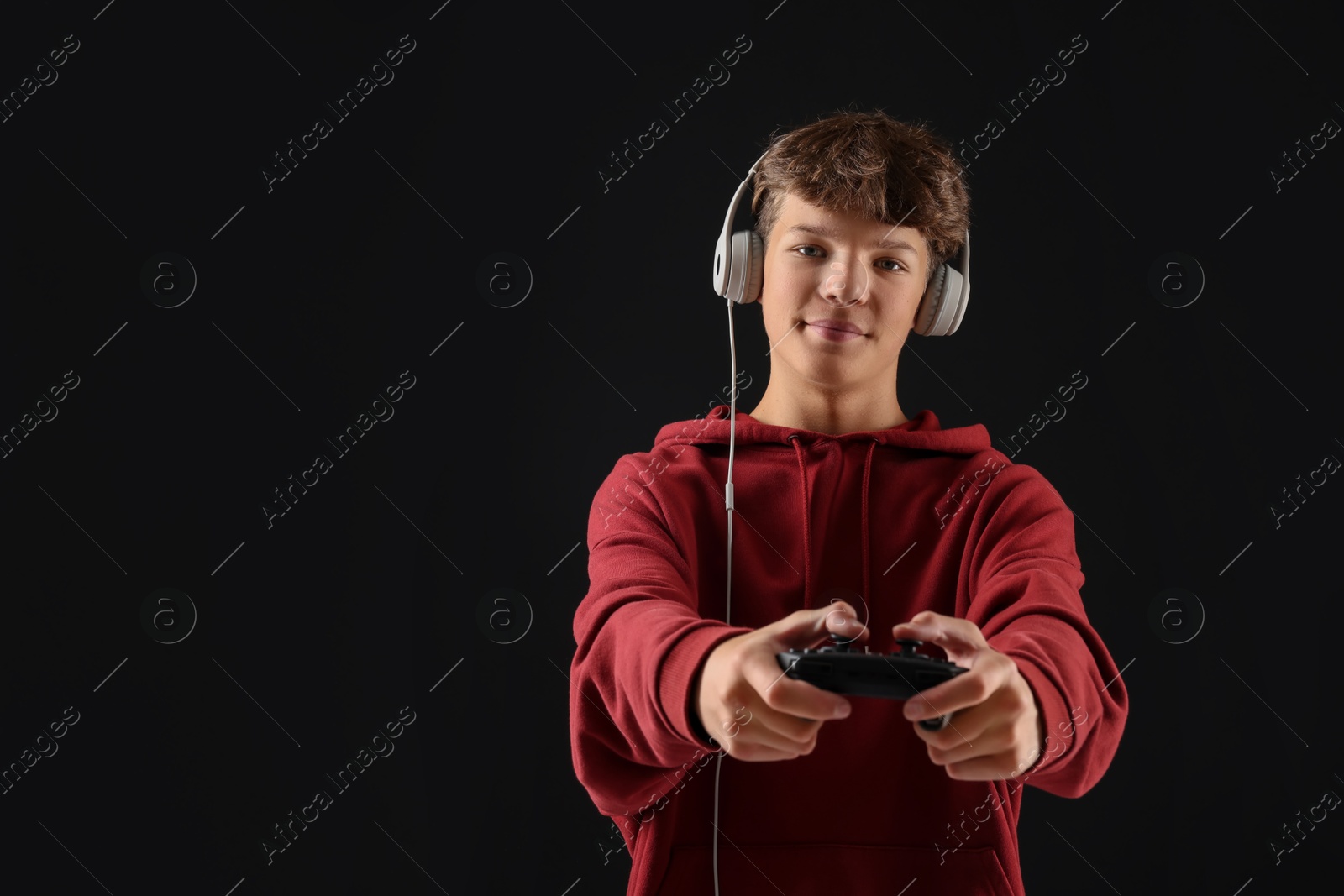 Photo of Teenage boy in headphones playing video game with controller on black background. Space for text