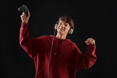 Happy teenage boy in headphones with controller on black background