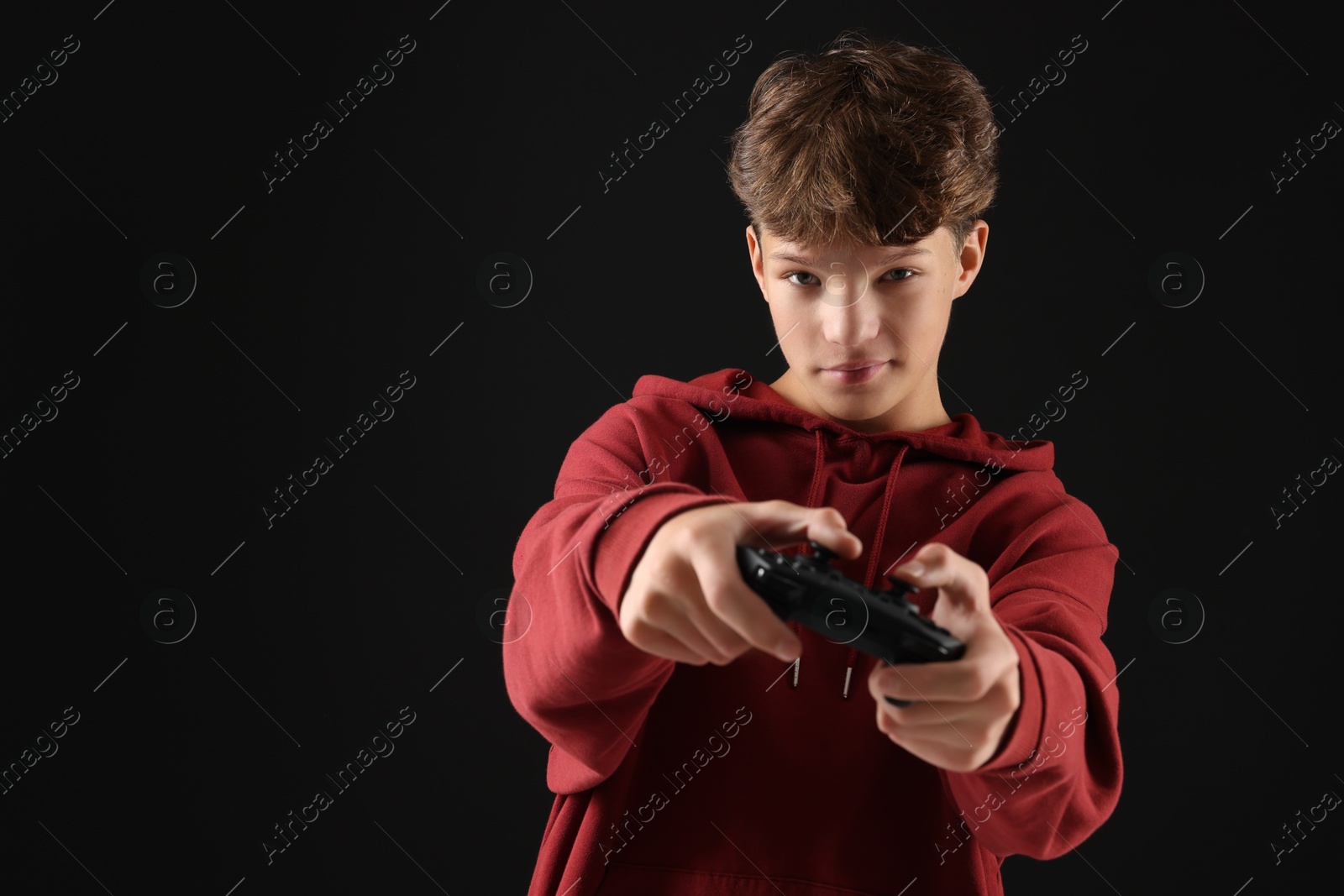 Photo of Teenage boy playing video game with controller on black background. Space for text