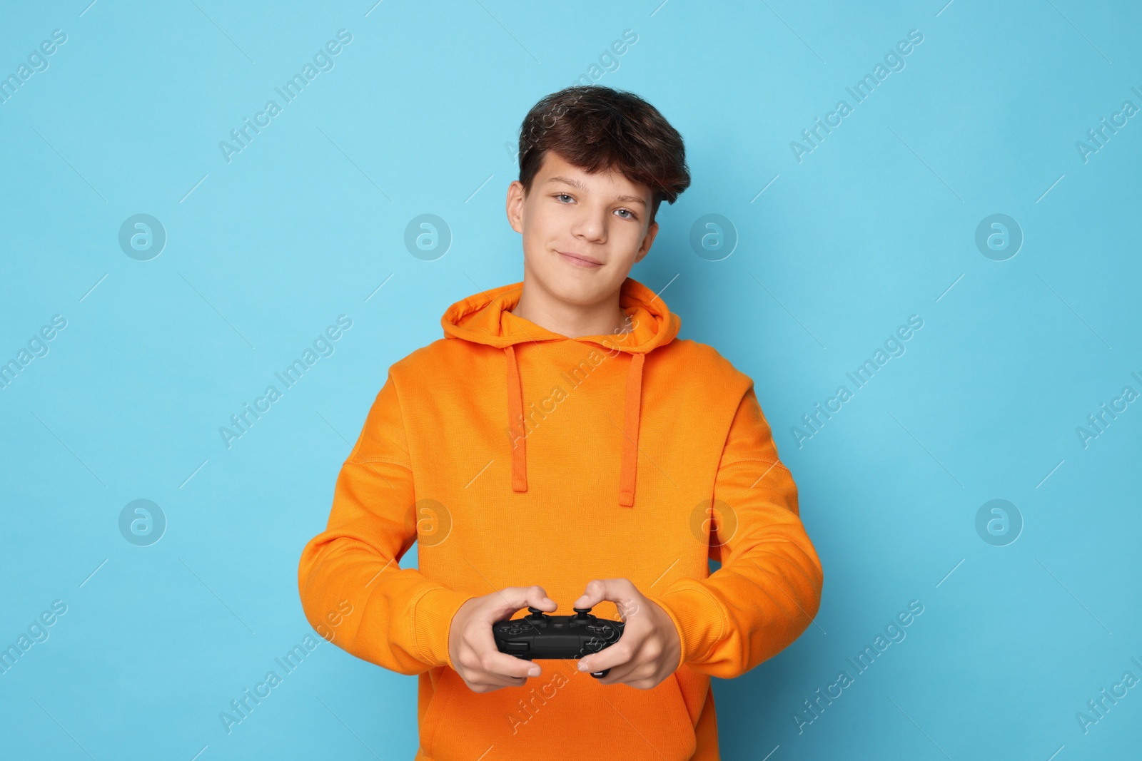 Photo of Teenage boy playing video game with controller on light blue background