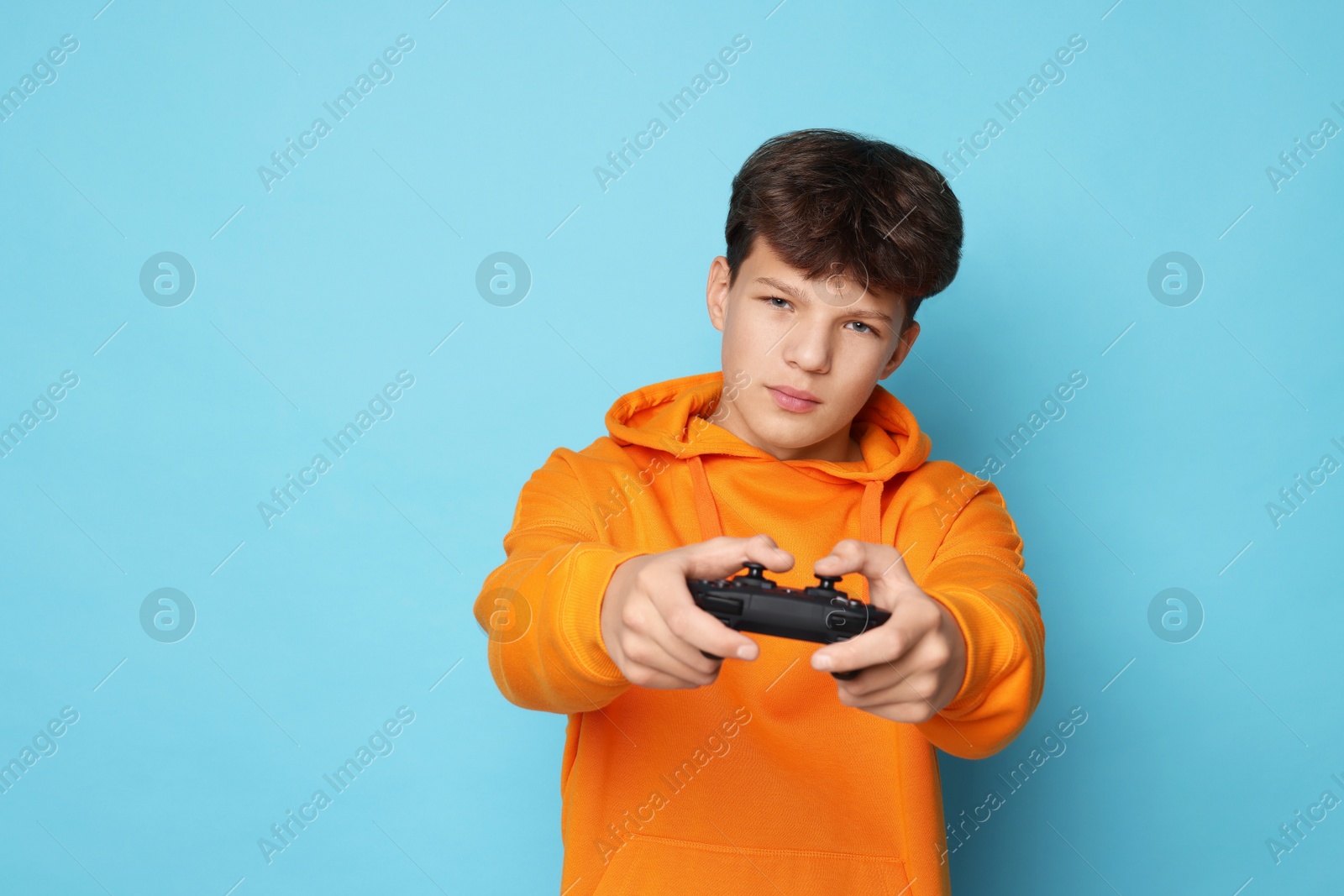 Photo of Teenage boy playing video game with controller on light blue background. Space for text