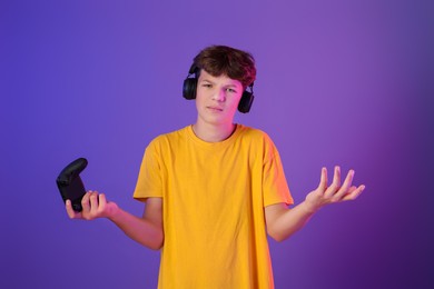 Photo of Teenage boy in headphones with controller on purple background