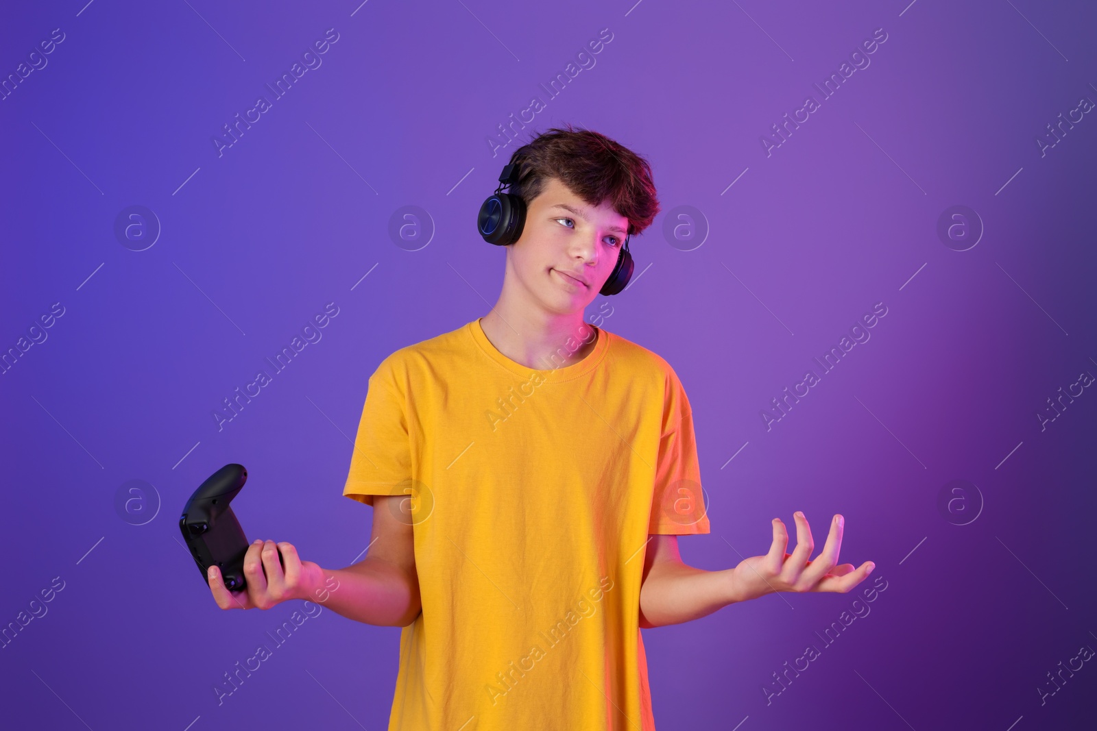 Photo of Teenage boy in headphones with controller on purple background