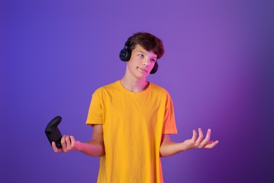 Teenage boy in headphones with controller on purple background