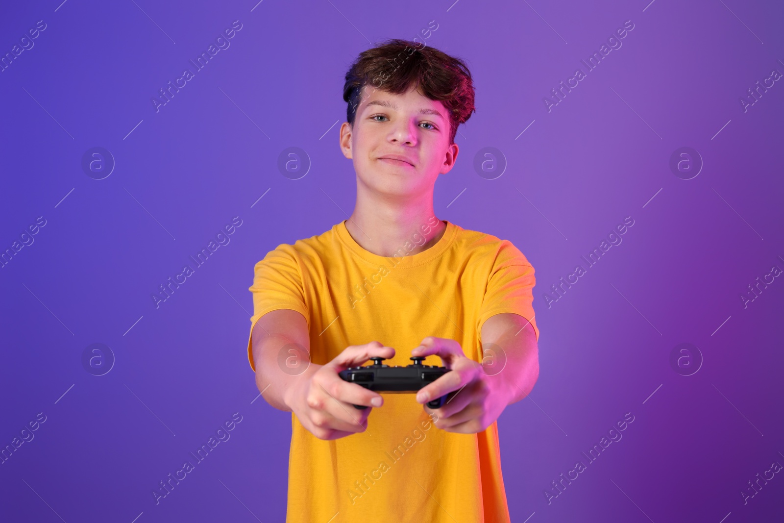 Photo of Teenage boy playing video game with controller on purple background