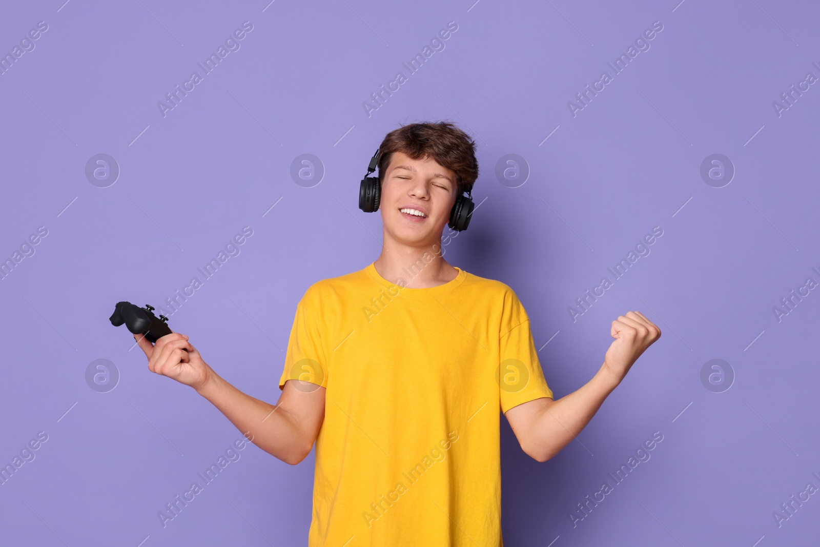 Photo of Happy teenage boy in headphones with controller on violet background