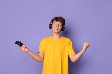 Happy teenage boy in headphones with controller on violet background