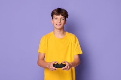 Happy teenage boy playing video game with controller on violet background