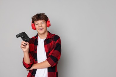 Happy teenage boy in headphones with controller on grey background. Space for text