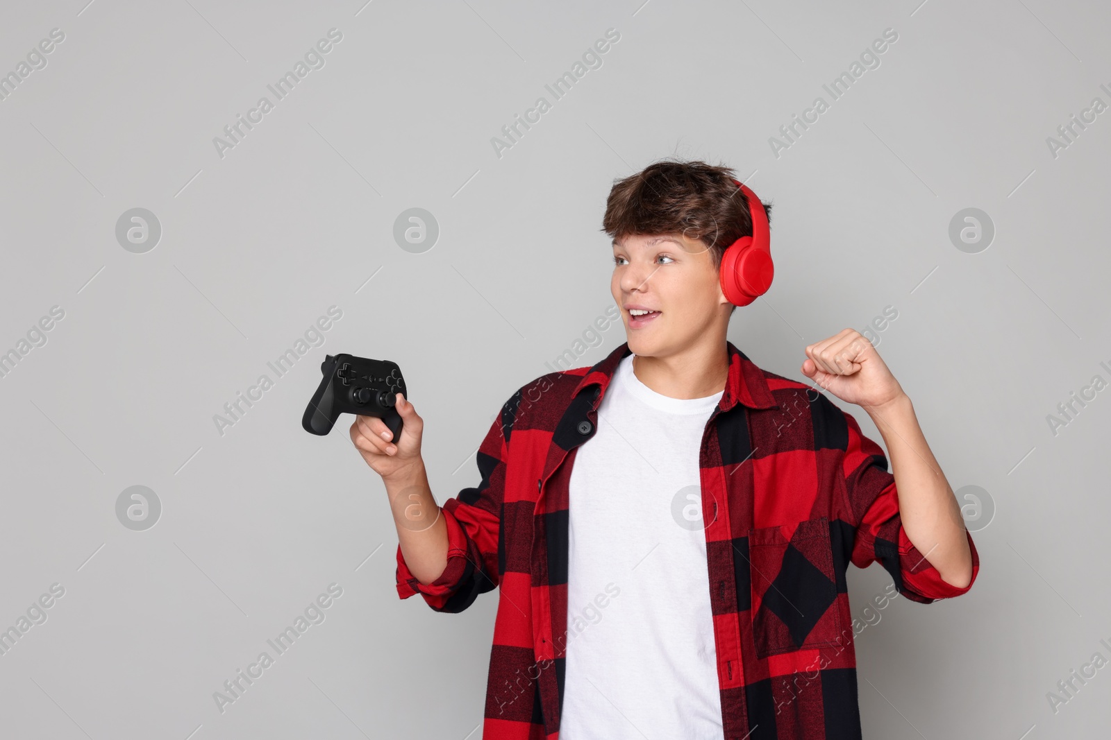 Photo of Happy teenage boy in headphones with controller on grey background. Space for text