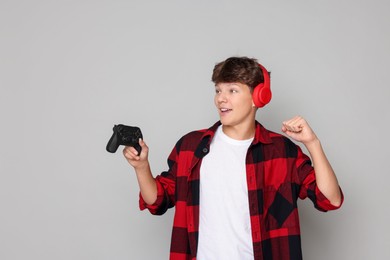 Photo of Happy teenage boy in headphones with controller on grey background. Space for text