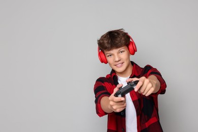 Photo of Happy teenage boy in headphones playing video game with controller on grey background. Space for text