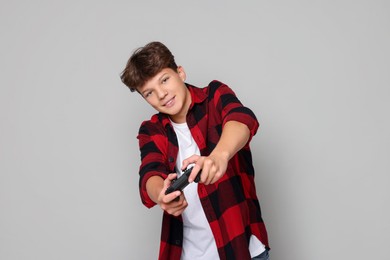 Happy teenage boy playing video game with controller on grey background