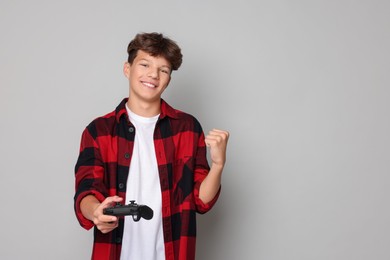 Happy teenage boy with controller on grey background. Space for text