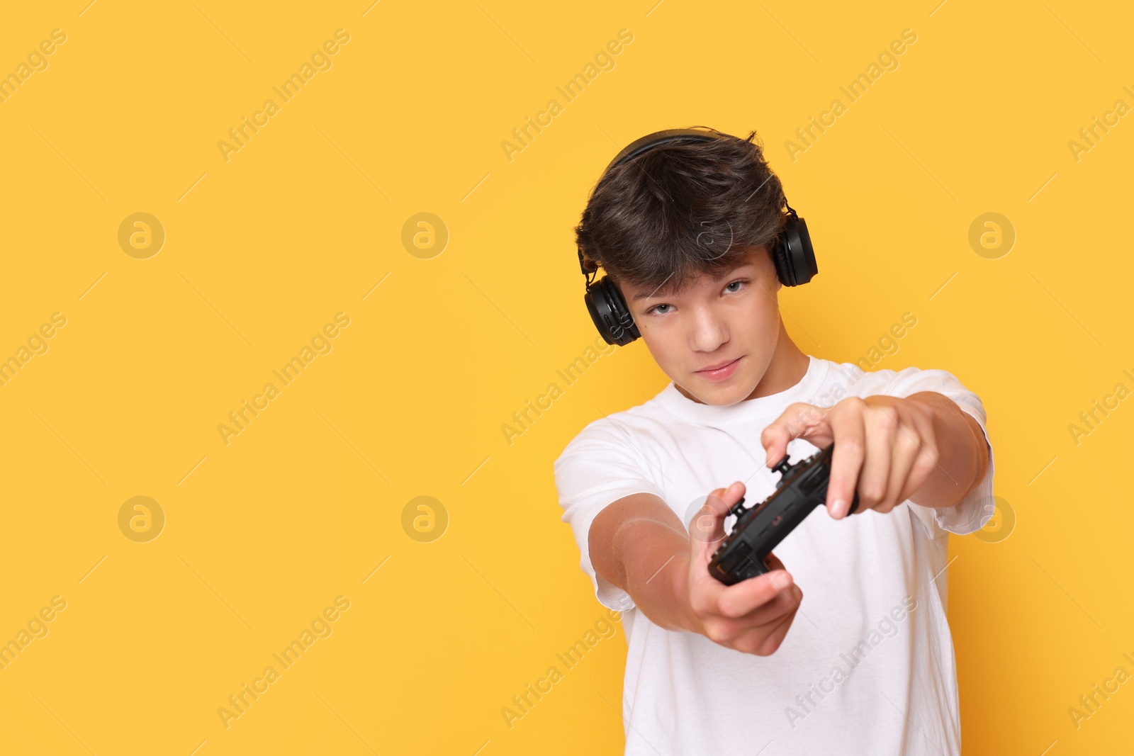 Photo of Teenage boy in headphones playing video game with controller on orange background. Space for text