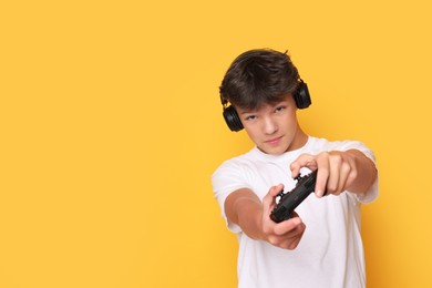 Photo of Teenage boy in headphones playing video game with controller on orange background. Space for text