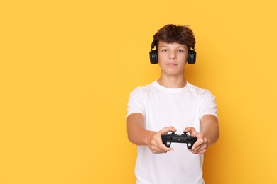 Photo of Teenage boy in headphones playing video game with controller on orange background. Space for text