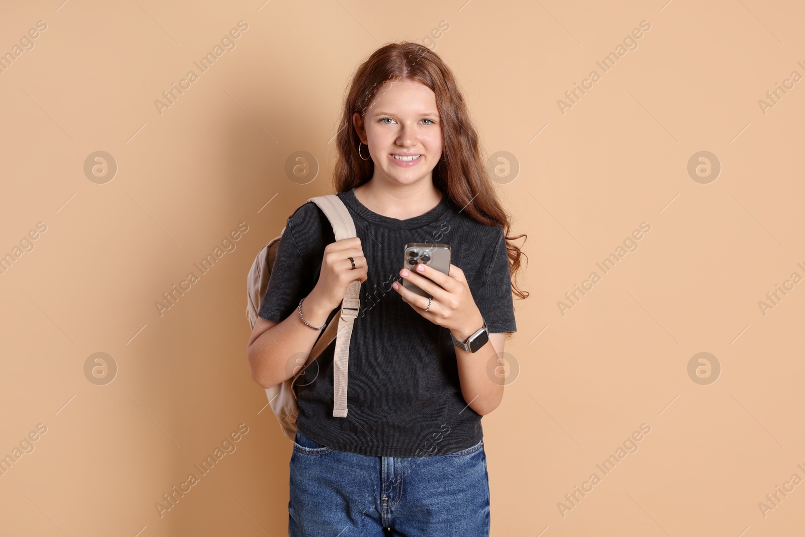 Photo of Smiling teenage girl with smartphone on beige background