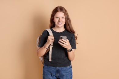 Smiling teenage girl with smartphone on beige background