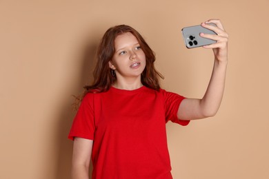 Photo of Cute teenage girl taking selfie on beige background