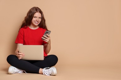 Smiling teenage girl with laptop and smartphone on beige background. Space for text