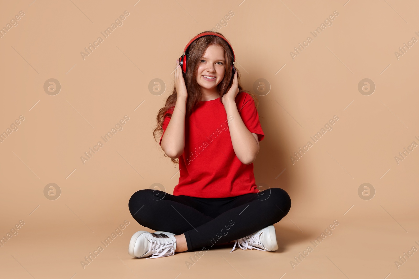 Photo of Smiling teenage girl in headphones listening to music on beige background