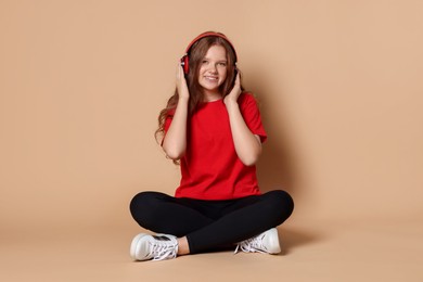 Smiling teenage girl in headphones listening to music on beige background