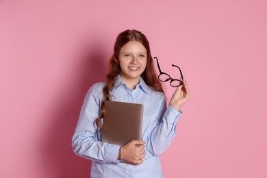 Photo of Smiling teenage girl with laptop and glasses on pink background