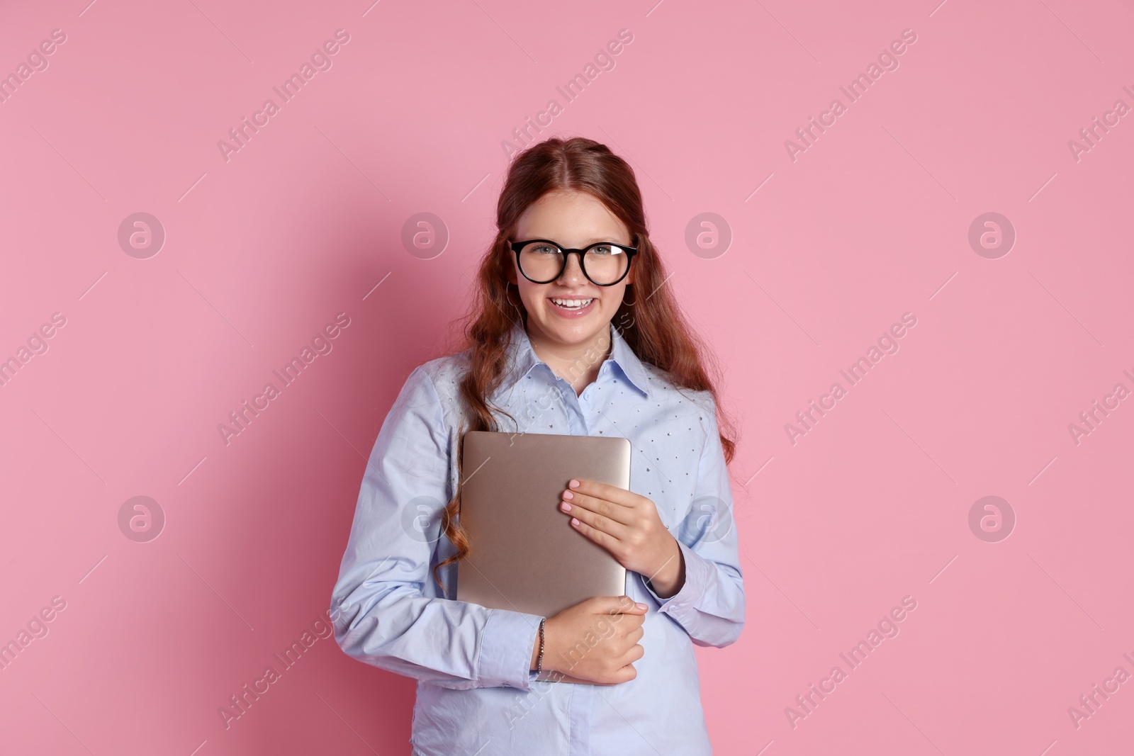 Photo of Happy teenage girl in glasses with laptop on pink background