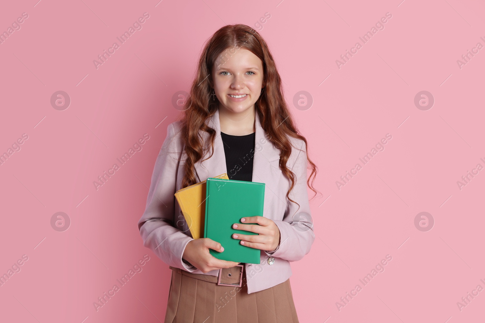 Photo of Smiling teenage girl with books on pink background