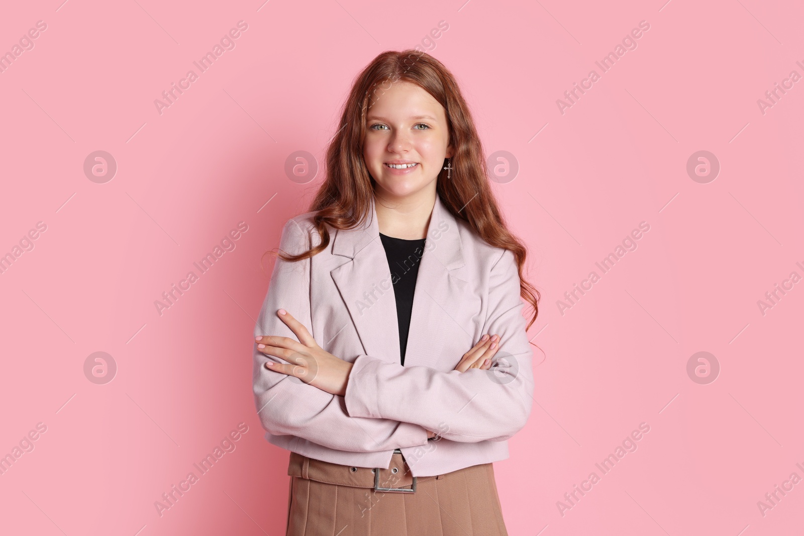 Photo of Smiling teenage girl with crossed arms on pink background