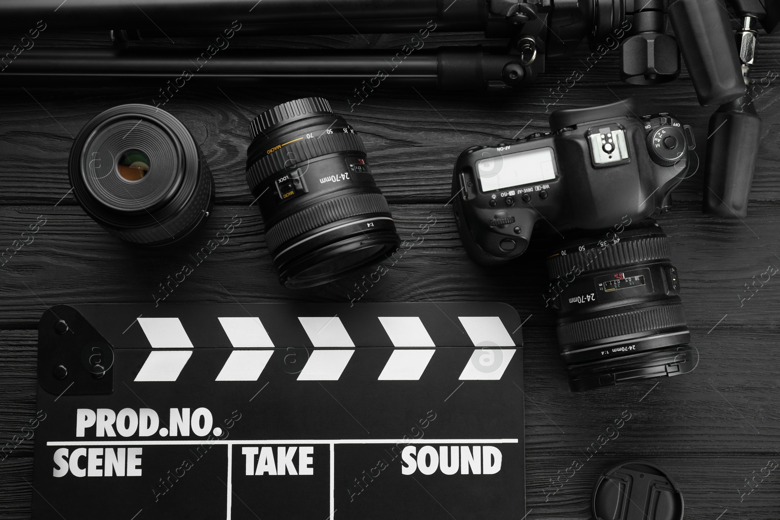 Photo of Movie clapper, camera and lens on black wooden table, flat lay