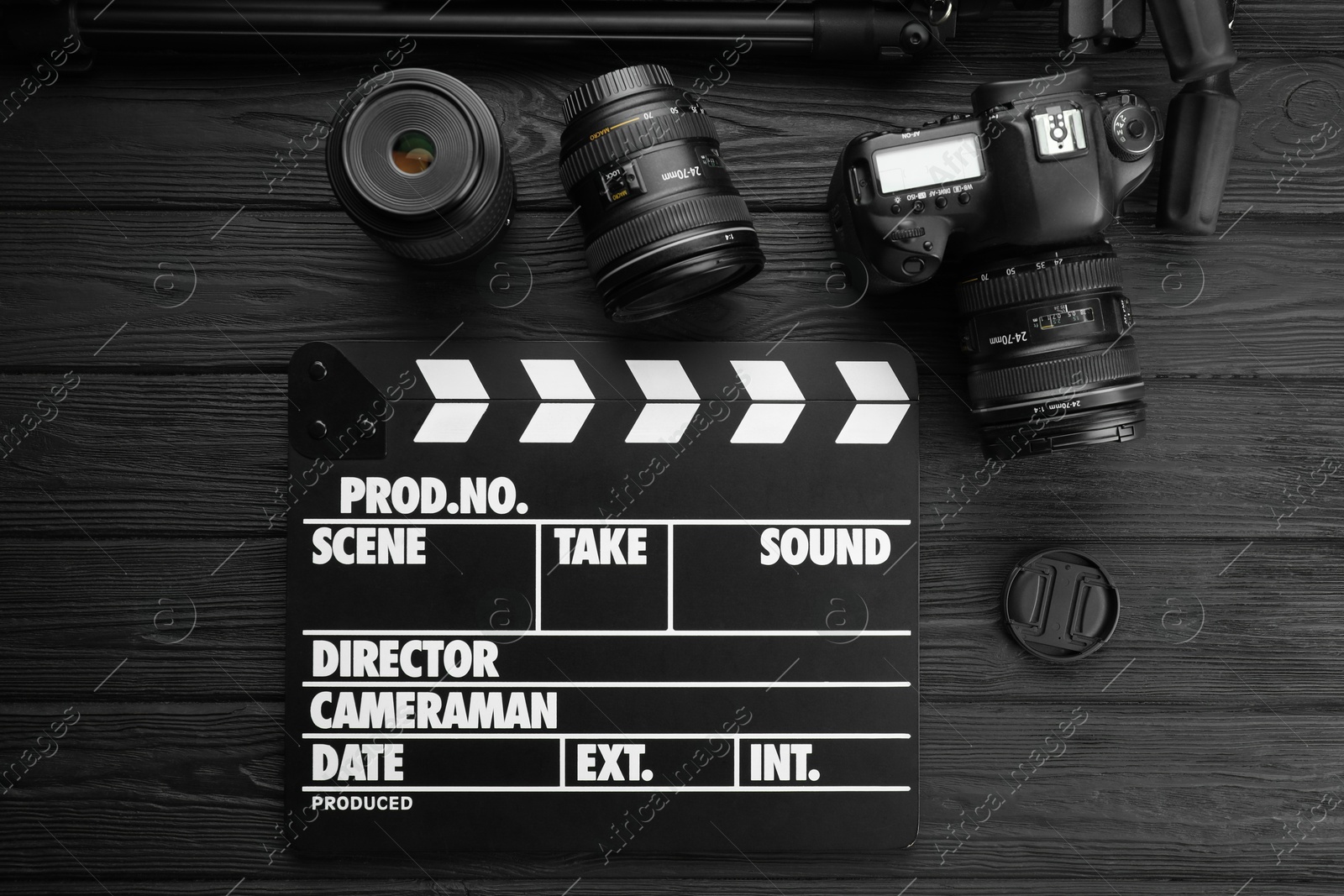 Photo of Movie clapper, camera and lens on black wooden table, flat lay