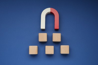 Photo of Magnet attracting wooden cubes on blue background, top view