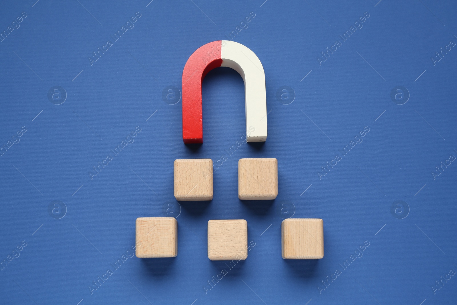 Photo of Magnet attracting wooden cubes on blue background, top view