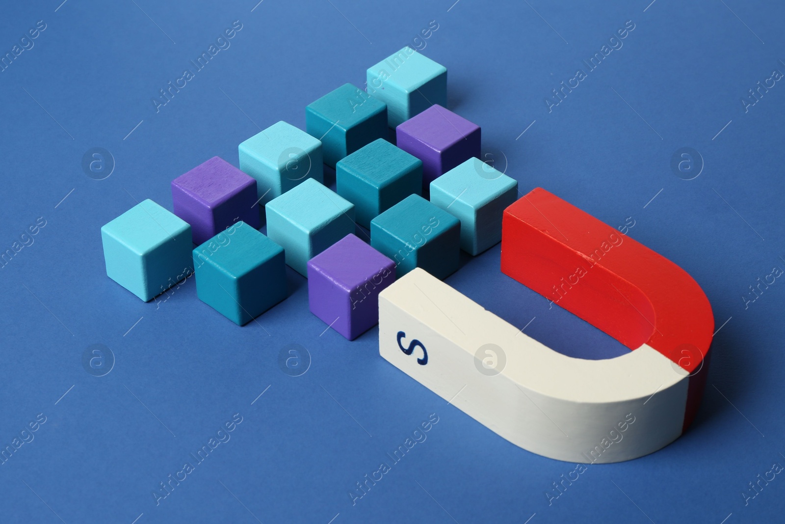 Photo of Magnet attracting colorful cubes on blue background, closeup