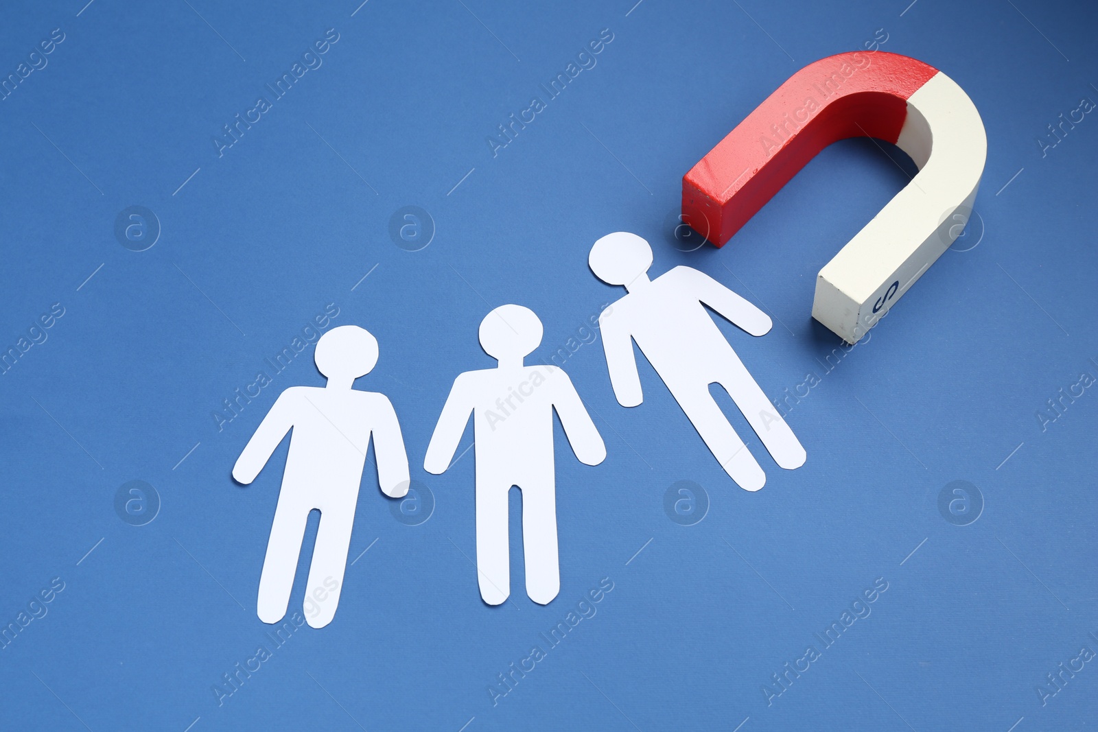 Photo of Magnet attracting paper people on blue background