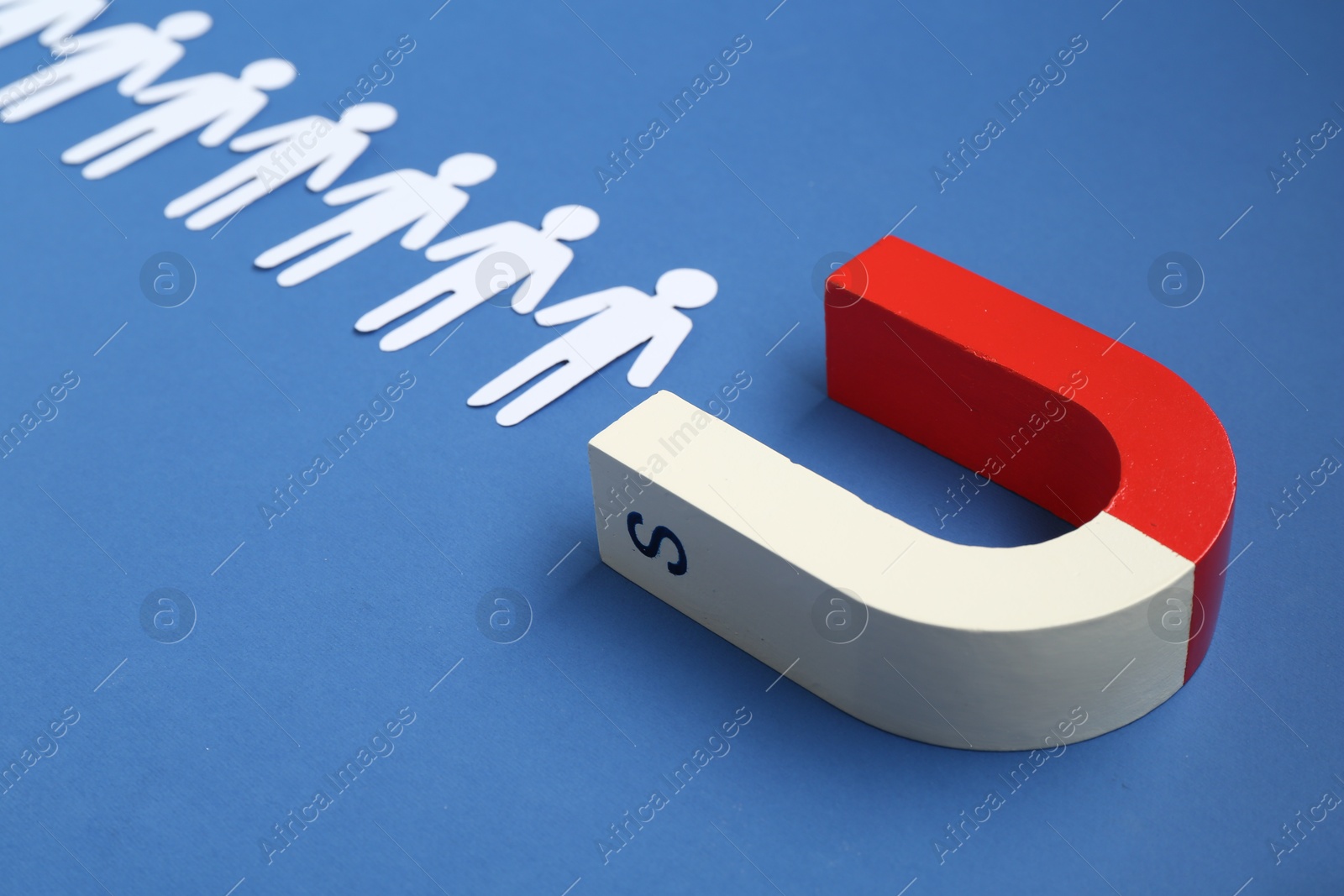 Photo of Magnet attracting paper people on blue background, closeup