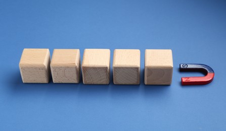 Photo of Magnet attracting wooden cubes on blue background