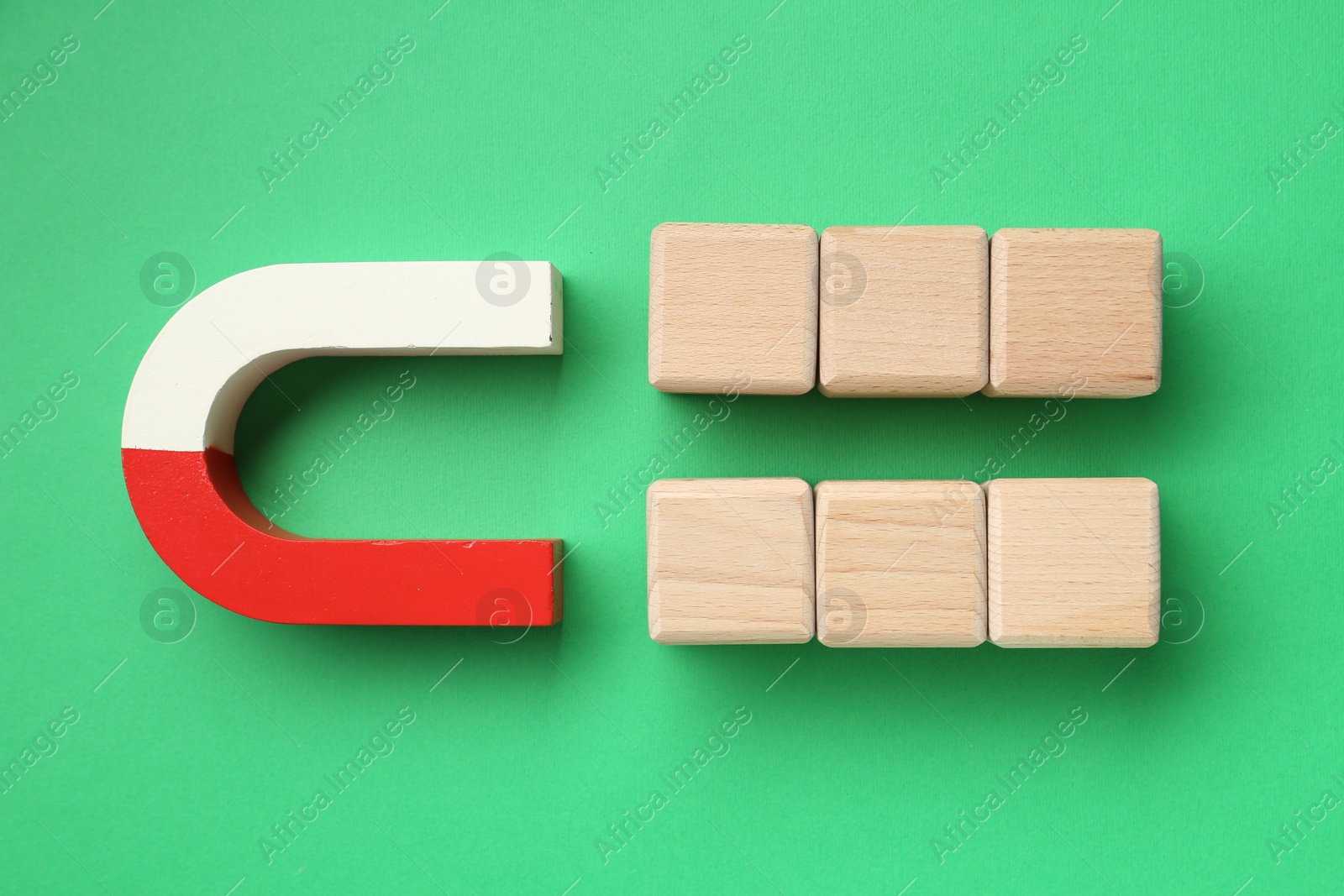 Photo of Magnet attracting wooden cubes on green background, flat lay