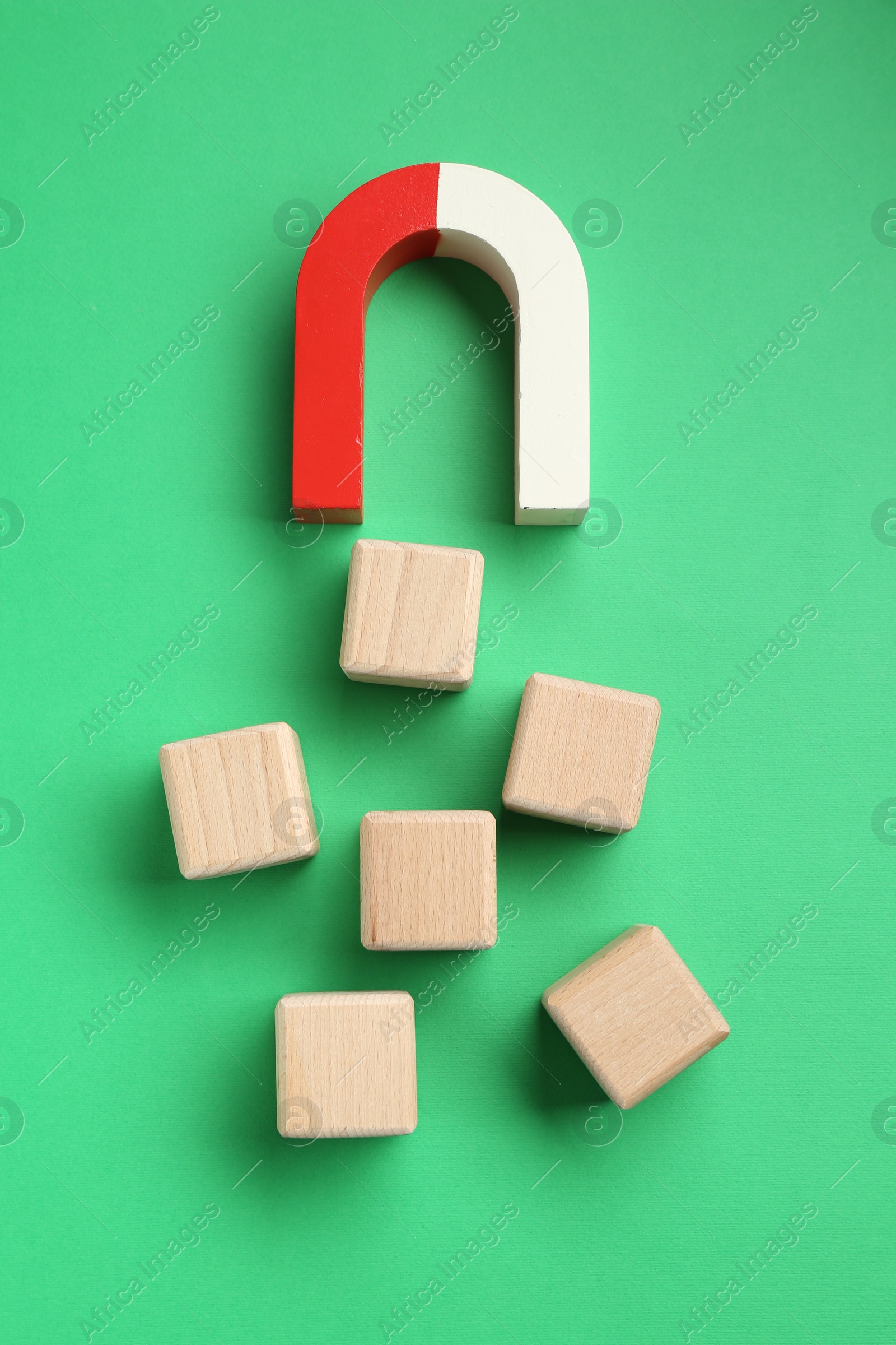 Photo of Magnet attracting wooden cubes on green background, flat lay