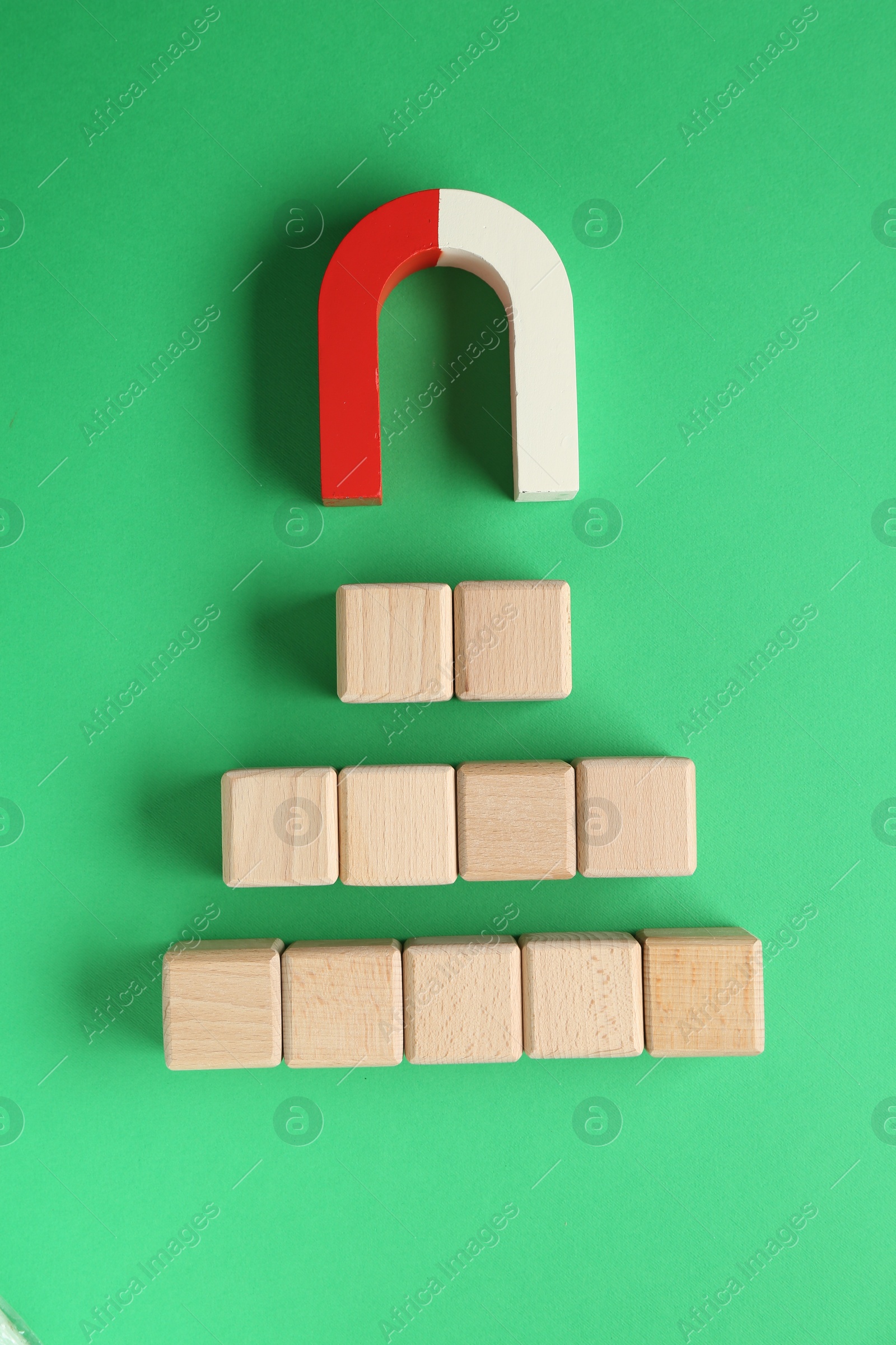 Photo of Magnet attracting wooden cubes on green background, flat lay